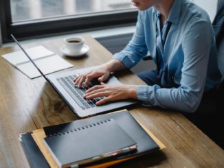 person in blue long sleeve shirt using macbook pro on brown wooden table