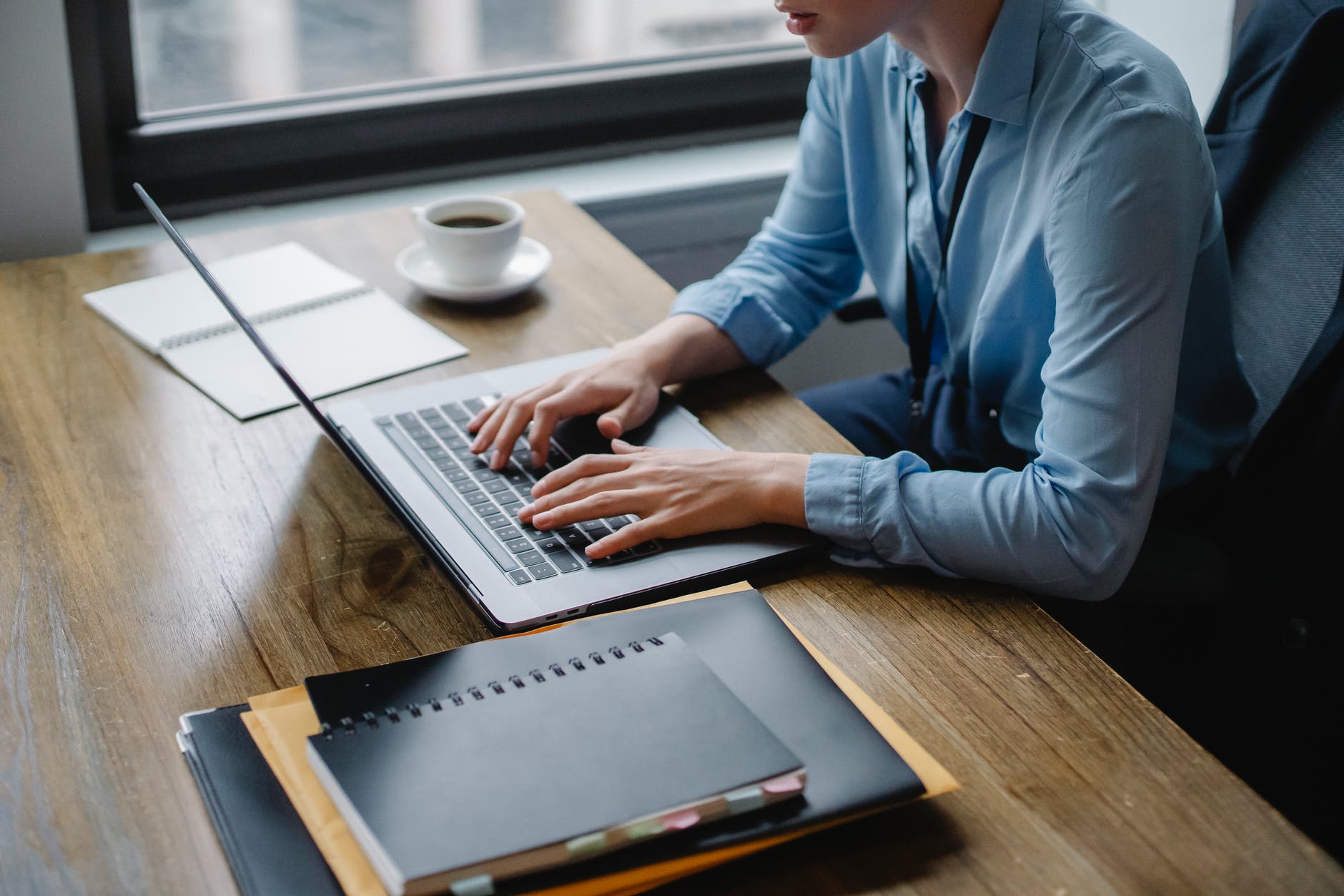 person in blue long sleeve shirt using macbook pro on brown wooden table